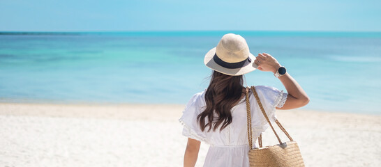 Happy traveler woman in white dress and hat enjoy beautiful sea view, young woman standing on sand...