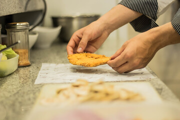 Hands of a cook preparing a schnitzel in the kitchen