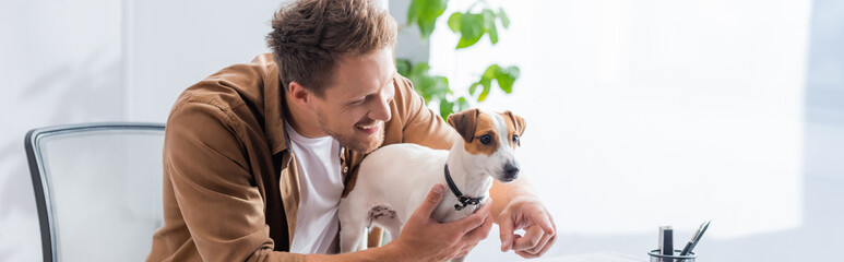 panoramic shot of young businessman pointing with finger near jack russell terrier dog in office