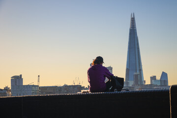 Fototapeta na wymiar Back view of a female sitting on Thames embankment with The Shard in the background