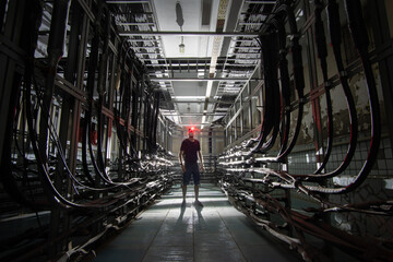 Silhouette of a man with a red lantern in medical mask in a dark cable tunnel with many cables....