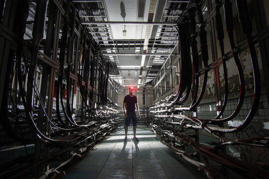 Silhouette of a man with a red lantern in medical mask in a dark cable tunnel with many cables. Cable cabinet of automatic telephone exchange.