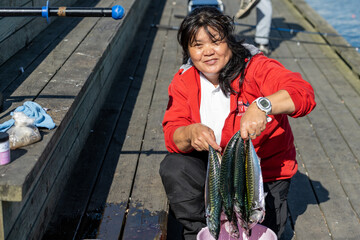 A smiling asian woman in her 50s shows a fresh catch of mackerel