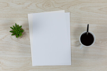 White sheet of papers surrounded by a plant and coffee on wood table
