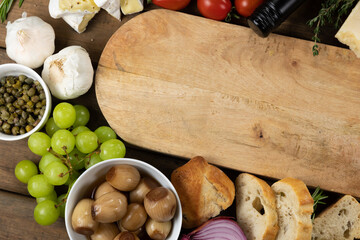 View of a wooden cutting board with bread, cheese, sausage, fruits and wine on a wooden surface