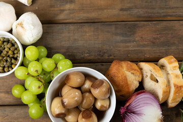 View of a wooden cutting board with bread, cheese, sausage, fruits and wine on a wooden surface