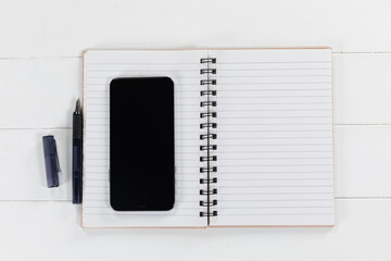 Fototapeta premium View of a black smartphone, a notebook and a black pen on plain white background
