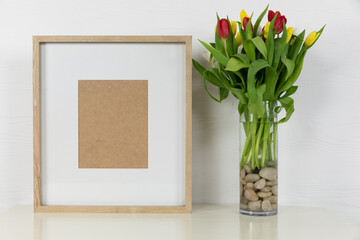 View of a picture frame, with red and yellow tulips placed in a glass vase on plain white background