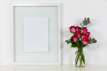 View of a picture frame, with pink roses placed in a glass vase on plain white background