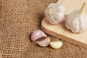 Garlic lies in a wicker basket on a brown wooden background.