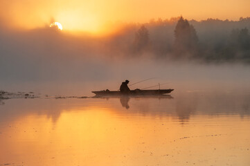 Silhouette image of a fisherman on a wooden boat. Sunrise over the river and fog