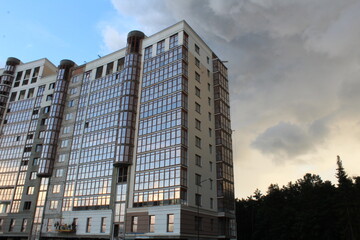 the building is a modern residential building complex with a glass facade during construction on the background of a blue sky with clouds illuminated by the sun at sunset