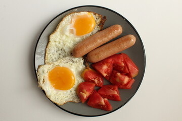 Breakfast eggs sausages salad vegetables red tomatoes on a gray plate on a white light background copy space