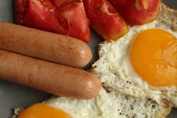 traditional English European Breakfast eggs sausage and salad vegetables red tomatoes on a gray plate on a black background close up side view
