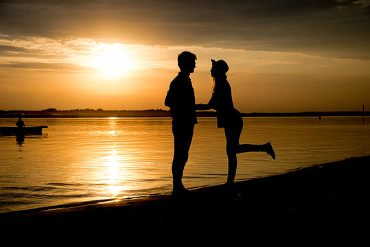 silhouette of a boy and a girl on the river bank at  sunset, gold water and sky