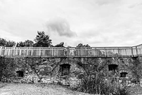 Brick walls with windows surrounding a courtyard with some plants, a wooden railing at the top at Schaesberg castle, cloudy day in Landgraaf, South Limburg in the Netherlands. Black and White image
