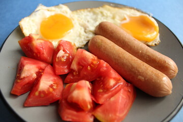 traditional European Breakfast eggs sausages sausages and salad vegetables red tomatoes on a grey plate on a blue background with copy space