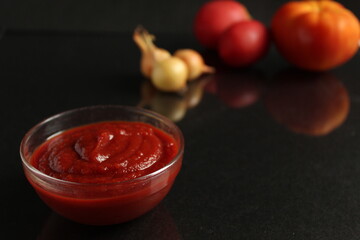 a glass saucepan with red tomato vegetable sauce stands on a black background in the background next to vegetables tomatoes red orange and onions in a yellow husk with Kopi space