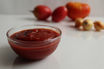 red tomato sauce ketchup in a glass salad bowl saucepan on a white background are vegetables in the background red tomatoes