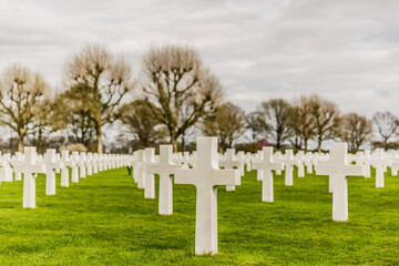 Crosses in the American Cemetery Margraten on a green grass in memory of soldiers killed in the war with a gray sky and trees in the background in South Limburg in the Netherlands Holland