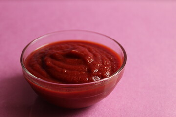 red tomato sauce in a glass sauce bowl stands on a pink fuchsia background with a copy space