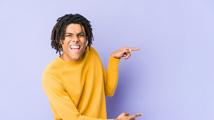 Young black man wearing rasta hairstyle pointing with forefingers to a copy space, expressing...