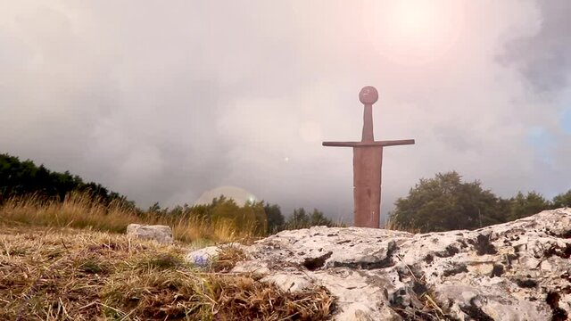 Sword in the stone scenic old rusted in landscape lens flare light effect, concept of power and adventure historical place