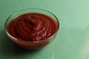 red tomato sauce in a glass saucepan bowl on a green background with a copy space food background