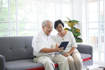 A happy senior Asian couple is using tablet and talking with family on webcam at home, retirement...