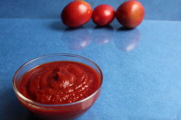 a glass bowl with a red tomato sauce the tomatoes are in the background behind on blue background with copy space food Italian cuisine