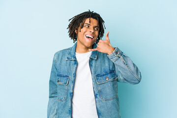 Young black man wearing a jeans jacket showing a mobile phone call gesture with fingers.