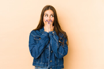 Young caucasian woman isolated en beige background thoughtful looking to a copy space covering mouth with hand.