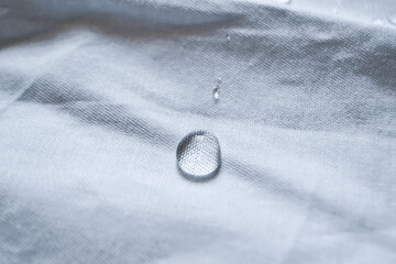 Pure water droplet shining in the light on a white fabric with folds