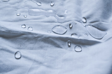 Water droplets on a white fabric drapery with folds shining in the light
