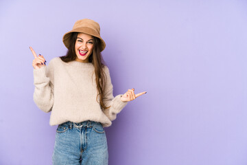 Young caucasian woman isolated on purple background pointing to different copy spaces, choosing one of them, showing with finger.