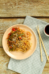 Funchoza with vegetables and mushrooms in a plate on a napkin next to sticks and soy sauce.