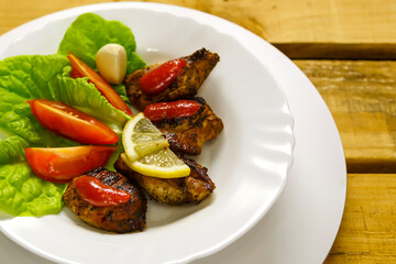 White plate with slices of grilled meat with lemon and tom.