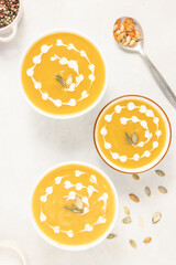 Pumpkin soup with rosemary herb, cream and pumpkin seeds on white background, top view, flat lay.