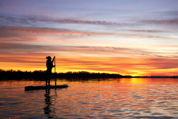 Silhouette of girl paddle on stand up paddle boarding (sup) on quiet river at winter sunset. Winter season and active leisure concept.