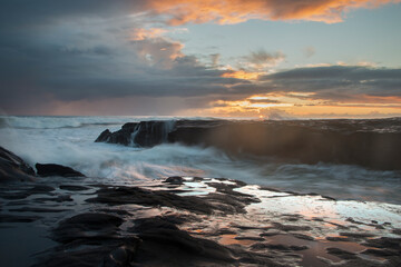 Sunset at Muriwai beach with splashing waves against the rocks