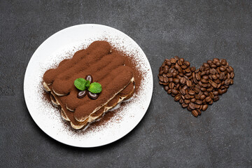 portion of Classic tiramisu dessert on ceramic plate and heart shaped coffee beans on concrete background