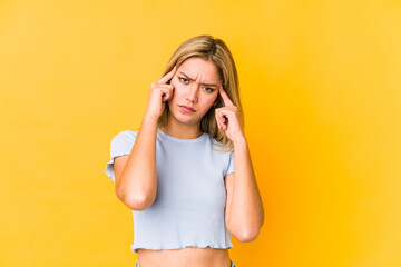 Young blonde caucasian woman isolated on a yellow background focused on a task, keeping forefingers pointing head.