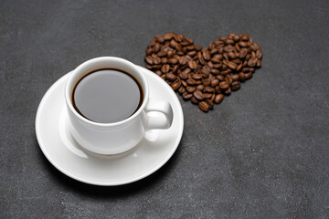 cup of fresh hot espresso coffee and heart shape made of beans on a dark concrete