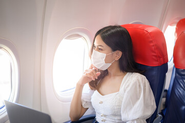 A young woman wearing face mask is using laptop onboard, New normal travel after covid-19 pandemic concept.