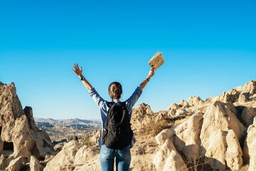 Obraz premium Woman with backpack raising hands with map standing on hill