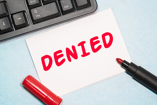 DENIED text on the business card written in red marker near the keyboard on a blue background