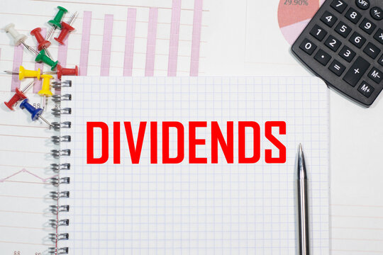 DIVIDENDS inscription on a notebook against the background of calculator charts, paper clips and pens