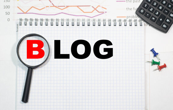 BLOG in a magnifying glass on a notepad against the background of graphs, calculator and paper clips.