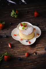 Fluffy souffle pancakes with cream and berries on white plate set on wooden table.