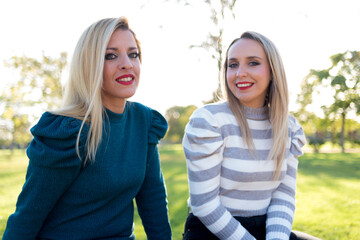 Blonde girls looking at the sunset happy. Sitting on a railing in the park.